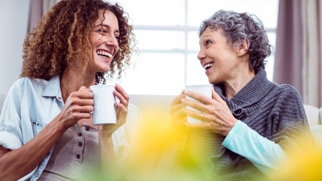 Smiling mother and daughter holding coffee mugs while conversing.